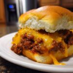 Close-up of a Sloppy Joe Slider topped with dripping, melted cheddar cheese on a white plate.