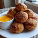 A pile of golden brown Soft Pretzel Bites with Beer Cheese Dip served on a white plate.