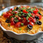 Close-up of a vibrant Southern 7-Layer Dip with Pimento Cheese Base topped with tomatoes, olives, and green onions.