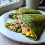 Close-up of folded Spinach Crepes with Ham and Egg Filling served on a white plate.