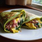 Two folded Spinach Crepes with Ham and Egg Filling showing melted cheese, ham, and scrambled eggs.