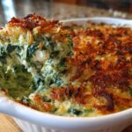 A spoonful of hot, cheesy Spinach and Kale Jalapeno Popper Dip being lifted from a white baking dish.