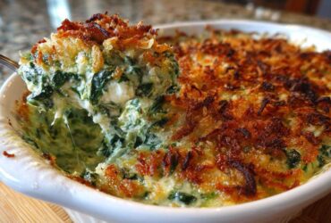 A spoonful of hot, cheesy Spinach and Kale Jalapeno Popper Dip being lifted from a white baking dish.