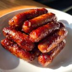 A pile of glossy, caramelized Sriracha Brown Sugar Smokies glistening under bright light on a white plate.