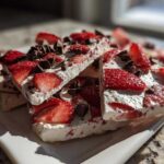 Close-up of stacked pieces of Strawberry Greek Yogurt Bark with dark chocolate chips on a white plate.