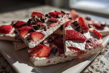 Close-up of stacked pieces of Strawberry Greek Yogurt Bark with dark chocolate chips on a white plate.