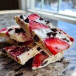 Stack of broken pieces of Strawberry Greek Yogurt Bark with dark chocolate chips on a granite counter.