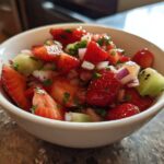 Close-up of vibrant Strawberry Kiwi Salsa featuring chopped strawberries, kiwi chunks, red onion, and herbs in a white bowl.