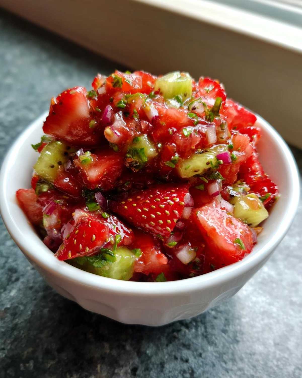 Close-up of vibrant Strawberry Kiwi Salsa featuring diced strawberries, kiwi, red onion, and herbs in a small white bowl.