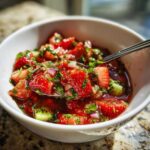 A spoonful of vibrant Strawberry Kiwi Salsa featuring chopped strawberries, kiwi chunks, red onion, and cilantro in a white bowl.
