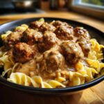 Close-up of Swedish Meatballs over Egg Noodles smothered in a rich, creamy brown sauce in a dark bowl.