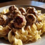 Close-up of savory Swedish meatballs covered in cream gravy served over wide egg noodles.