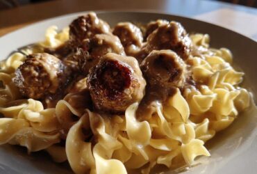 Close-up of savory Swedish meatballs covered in cream gravy served over wide egg noodles.