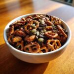 Close-up of a white bowl filled with Sweet and Salty Gameday Trail Mix, featuring glazed pretzels and pumpkin seeds.