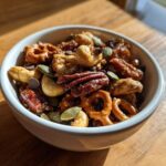 Close-up of a white bowl filled with Sweet and Salty Gameday Trail Mix, featuring pecans, cashews, pretzels, and chocolate chips.