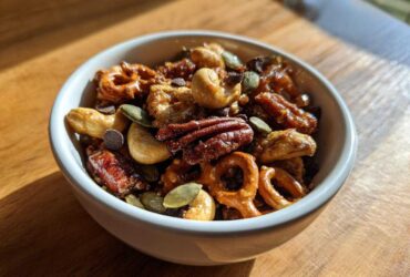 Close-up of a white bowl filled with Sweet and Salty Gameday Trail Mix, featuring pecans, cashews, pretzels, and chocolate chips.