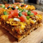 A thick slice of Taco Pizza with Corn Chip Topping showing seasoned beef, melted cheese, and fresh diced tomatoes and green onions.