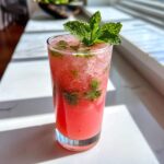 A tall glass filled with a bright pink Watermelon Mint Refresher, topped with crushed ice and a large sprig of fresh mint.