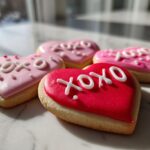 Close-up of heart-shaped XOXO Frosted Sugar Cookies with pink and red icing.