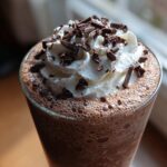 Close-up of a tall glass of frozen hot chocolate topped with whipped cream and chocolate shavings.