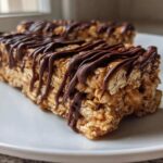 Two homemade protein bars made with oats, drizzled heavily with melted dark chocolate, resting on a white plate.