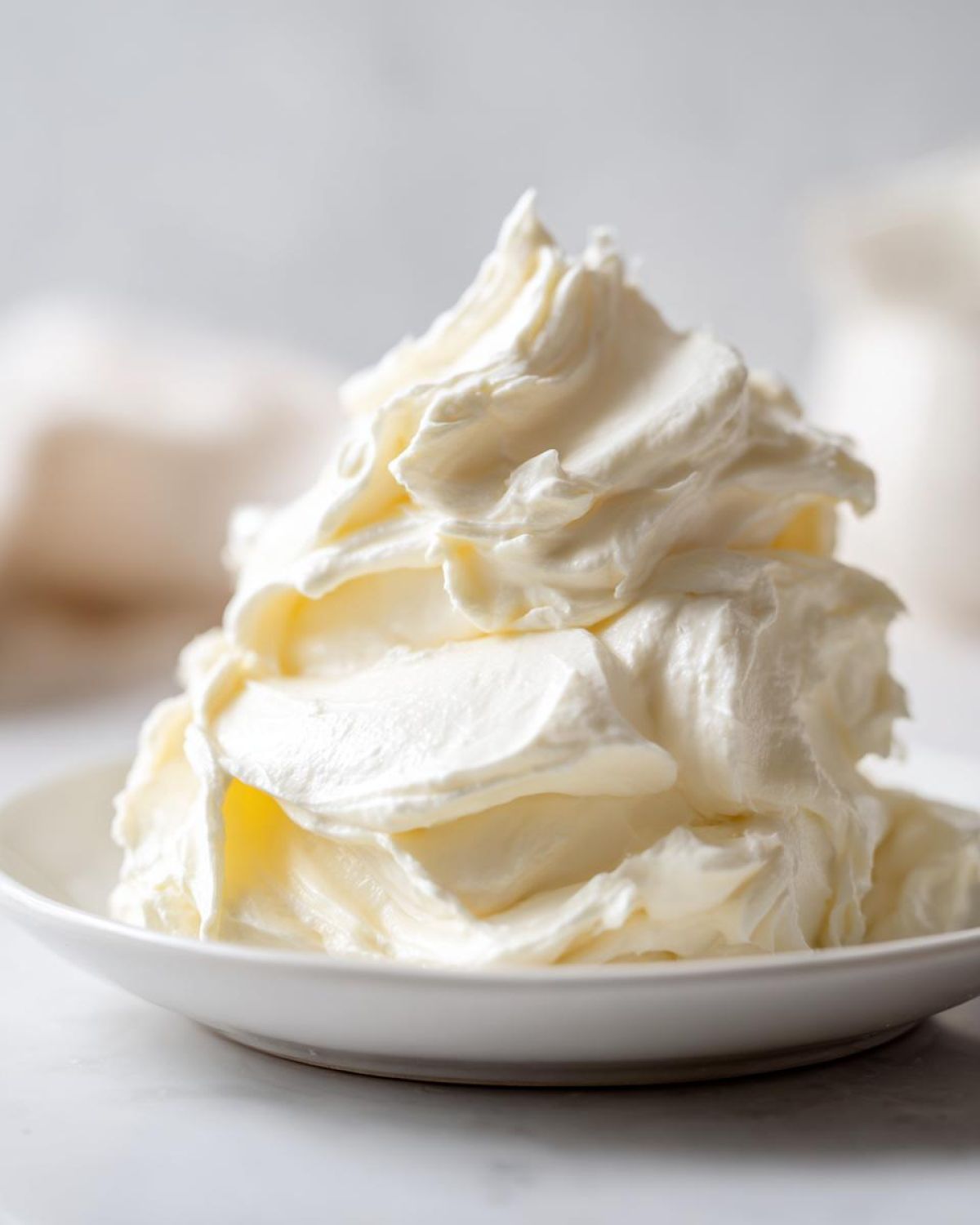 A close-up of perfectly whipped, fluffy cream cheese frosting piled high on a small white plate.