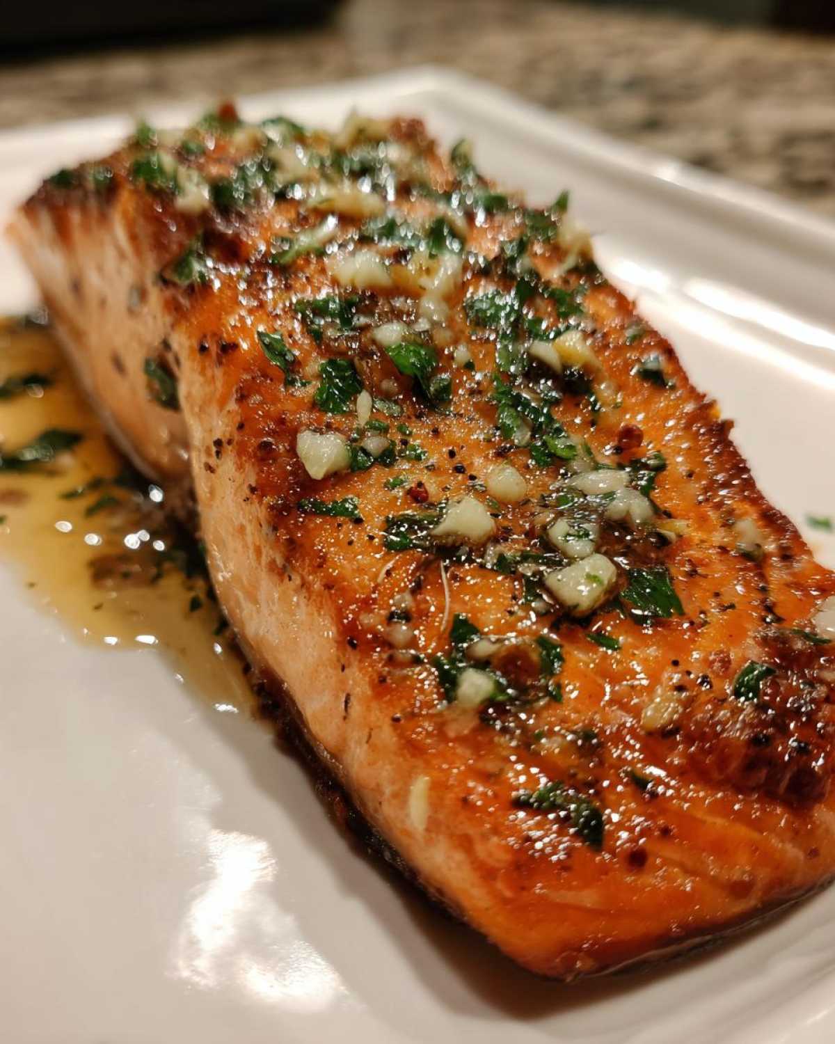 Close-up of a glistening, perfectly cooked air fryer salmon fillet topped with minced garlic and parsley.