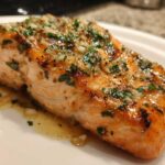 Close-up of a glistening, cooked fillet of air fryer salmon topped with minced garlic and fresh parsley.