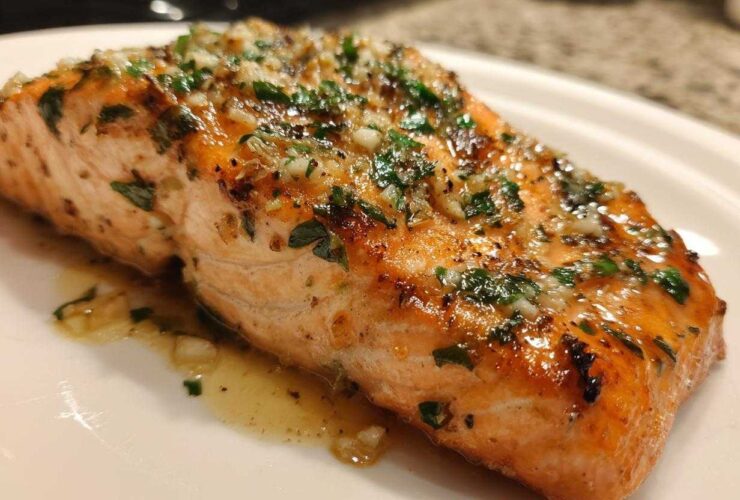 Close-up of a glistening, cooked fillet of air fryer salmon topped with minced garlic and fresh parsley.