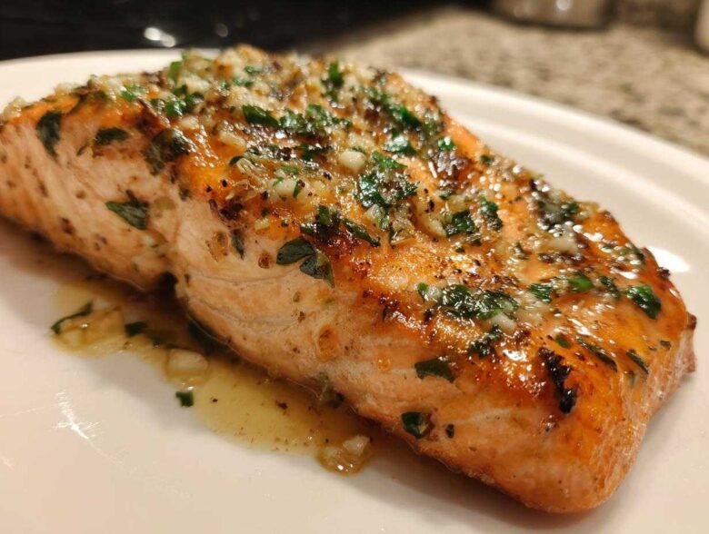 Close-up of a glistening, cooked fillet of air fryer salmon topped with minced garlic and fresh parsley.
