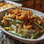 A close-up of a serving dish filled with creamy green bean casserole topped generously with crispy fried onions.