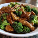 Close-up of tender chicken and bright green broccoli florets coated in a rich brown sauce for chicken and broccoli.