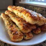 A close-up stack of golden, cheesy, and herb-topped breadsticks ready to eat.