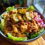A close-up of a delicious cheeseburger bowl featuring seasoned ground beef, lettuce, pickles, and special sauce.