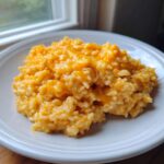A close-up of a serving of creamy, bright orange cheesy rice on a white plate.