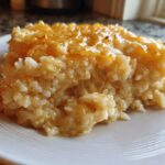 A close-up serving of amazing cheesy rice, topped with melted golden cheddar cheese, on a white plate.