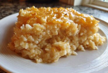 A close-up serving of amazing cheesy rice, topped with melted golden cheddar cheese, on a white plate.