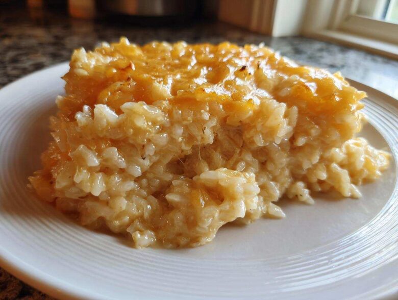 A close-up serving of amazing cheesy rice, topped with melted golden cheddar cheese, on a white plate.
