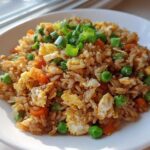 A close-up of a bowl of amazing chicken fried rice garnished with green onions, peas, and scrambled egg.