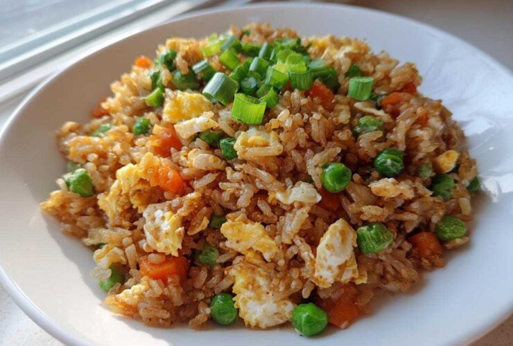 A close-up of a bowl of amazing chicken fried rice garnished with green onions, peas, and scrambled egg.