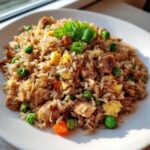 A close-up of amazing chicken fried rice featuring rice, scrambled egg, peas, carrots, and topped with green onions.