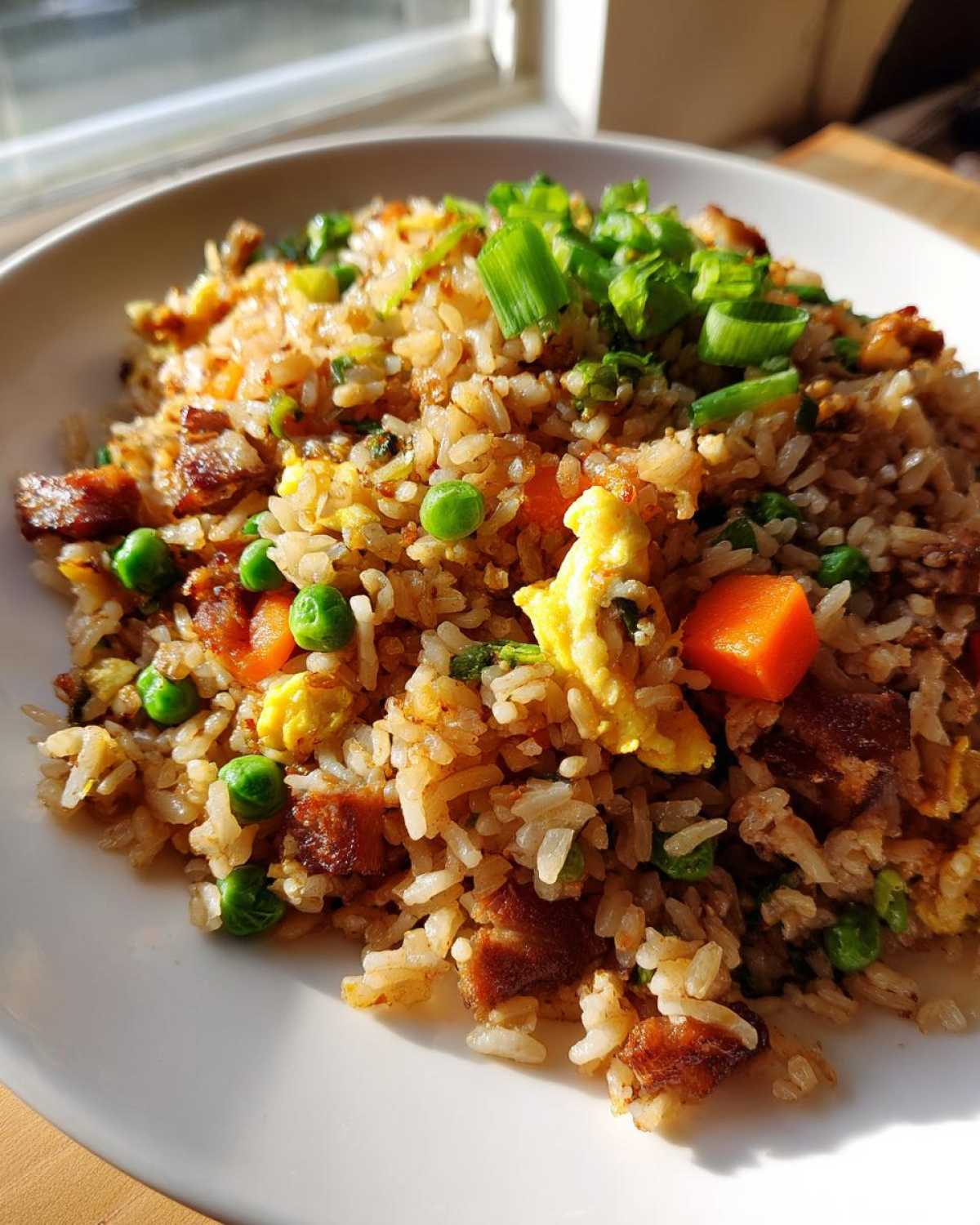 Close-up of a bowl of amazing chicken fried rice, featuring scrambled egg, diced carrots, peas, and green onions.