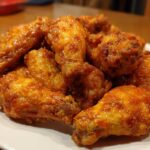 A pile of perfectly cooked, glossy, orange-glazed chicken wings stacked on a white plate.