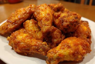 A pile of perfectly cooked, glossy, orange-glazed chicken wings stacked on a white plate.