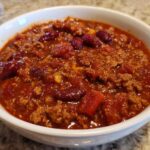 Close-up of a white bowl filled with rich, thick crockpot chili featuring ground meat and kidney beans.