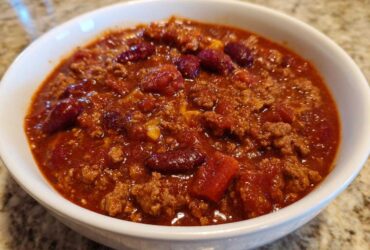 Close-up of a white bowl filled with rich, thick crockpot chili featuring ground meat and kidney beans.