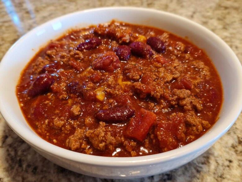 Close-up of a white bowl filled with rich, thick crockpot chili featuring ground meat and kidney beans.