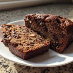 Two slices of moist, dark date nut bread packed with dates and walnuts, served on a white plate.