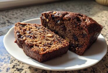 Two slices of moist, dark date nut bread packed with dates and walnuts, served on a white plate.