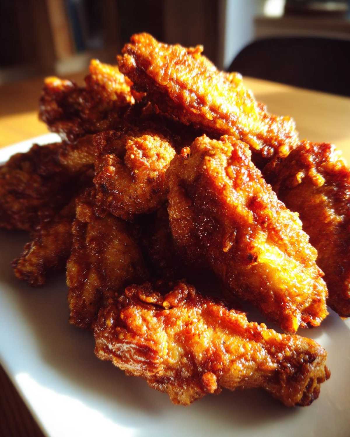 Close-up of a pile of perfectly golden and crispy fried chicken wings glistening under bright light.